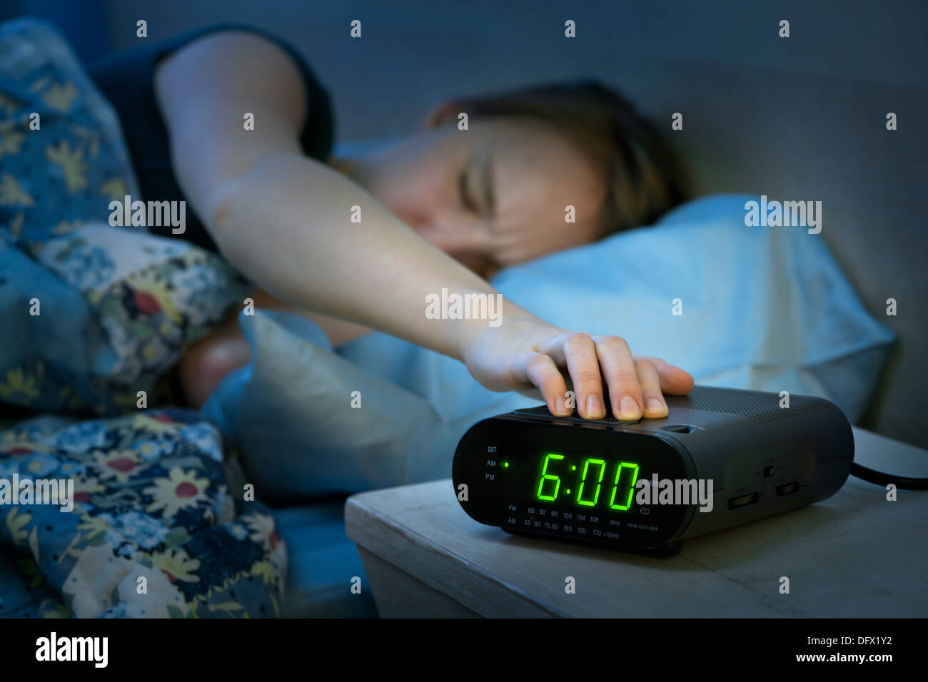 Junge Frau Drücken der Snooze-Taste am frühen Morgen digital Radiowecker Stockfoto