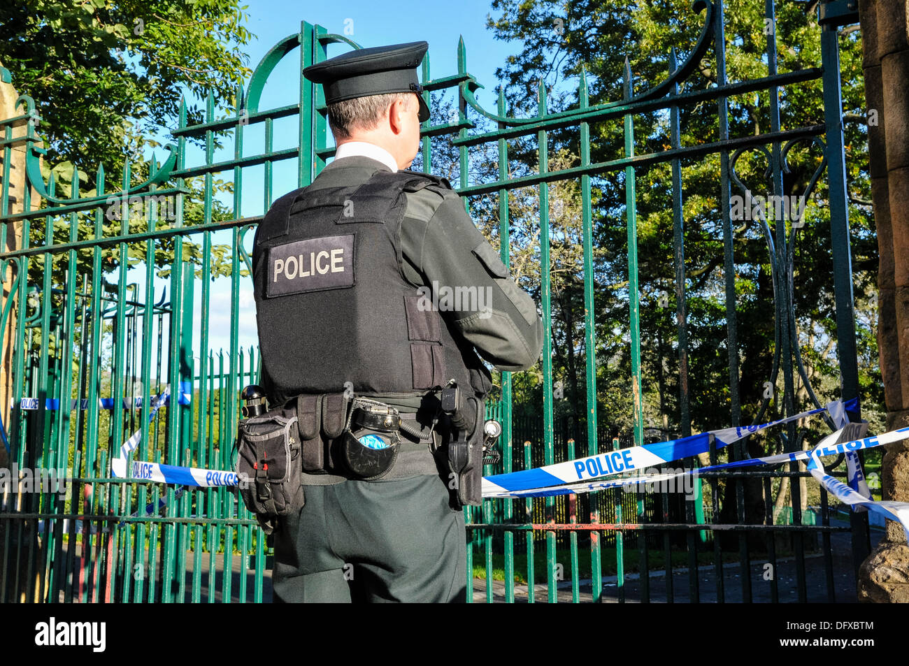 Ein Polizist aus der PSNI Wachen das Tor von einem Park, der Polizei Band über Es folgt ein Verbrechen Stockfoto