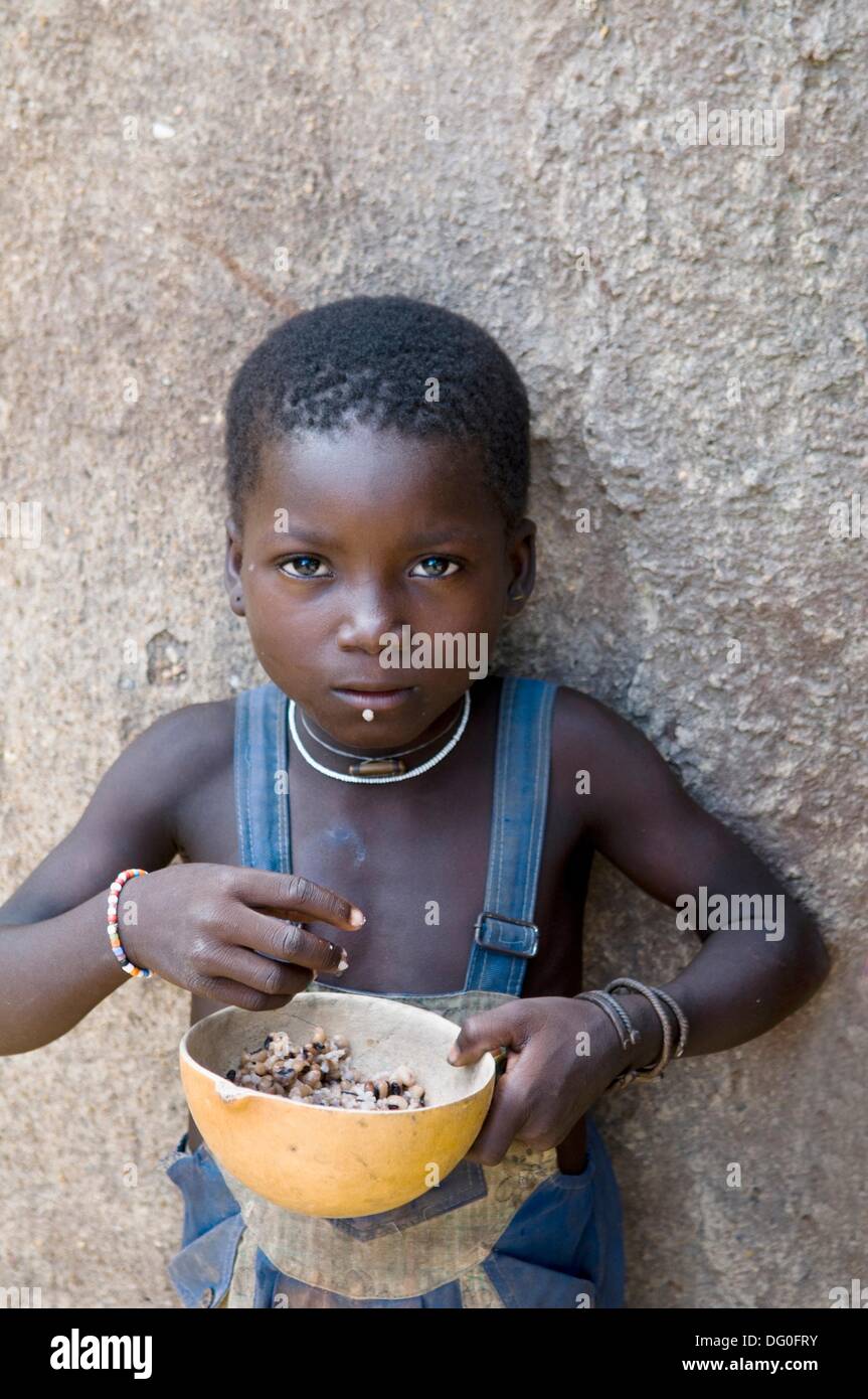 Eine niedliche kleine Mädchen Essen von ihrem Haus in einem kleinen Dorf im Norden Benins nahe der Grenze zu Togo Stockfoto