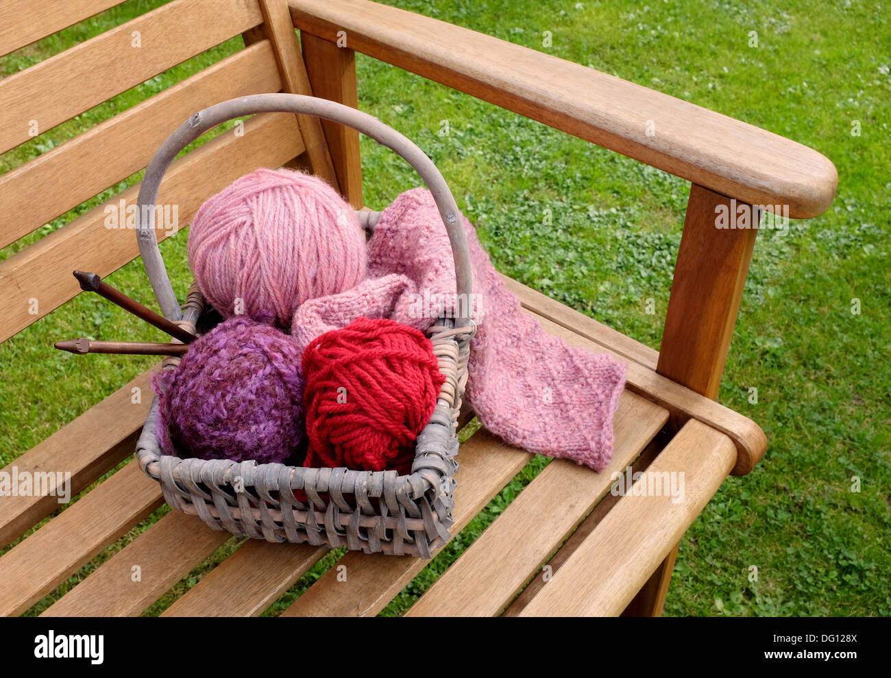 Handwerk-Korb mit gemusterten stricken, Kugeln aus Wolle und Holz Nadeln auf eine Gartenbank Stockfoto