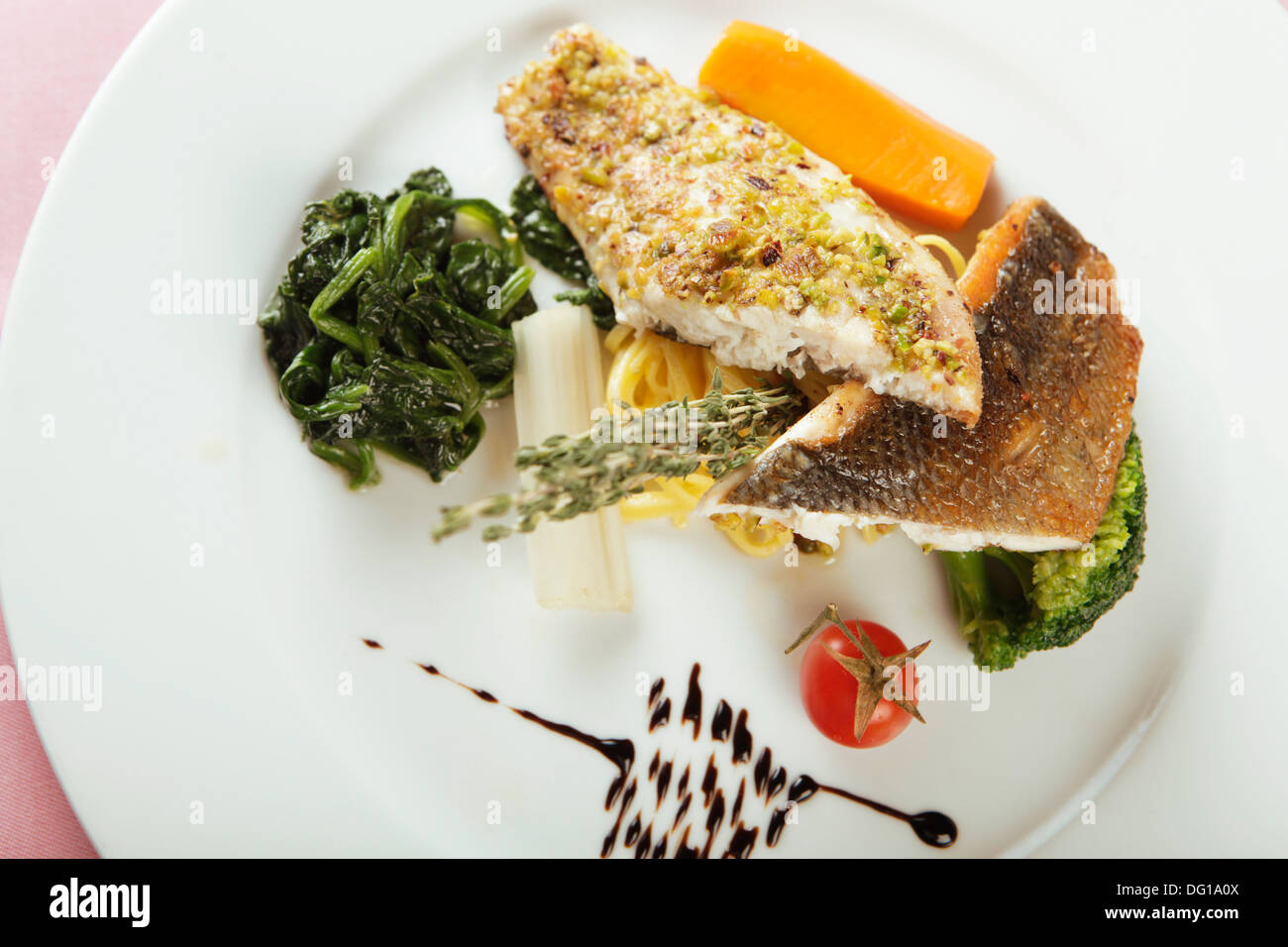 Fischgericht mit Spinat, eine Auswahl von Fischfilets auf einer Platte, mit Gemüse und Kräutern garniert serviert Stockfoto