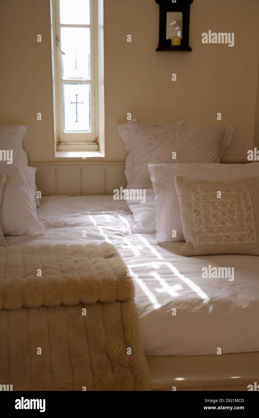 Creme-weiße Kissen mit Beige werfen auf eingebauten Bett unten schmale Fenster mit eingravierte Kreuze im Kleinstaat Schlafzimmer Stockfoto