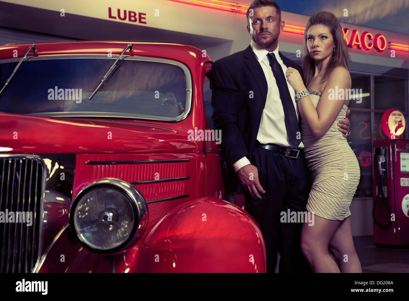 Gut gekleideter Mann und Frau neben roten Oldtimer vor Tankstelle Stockfoto