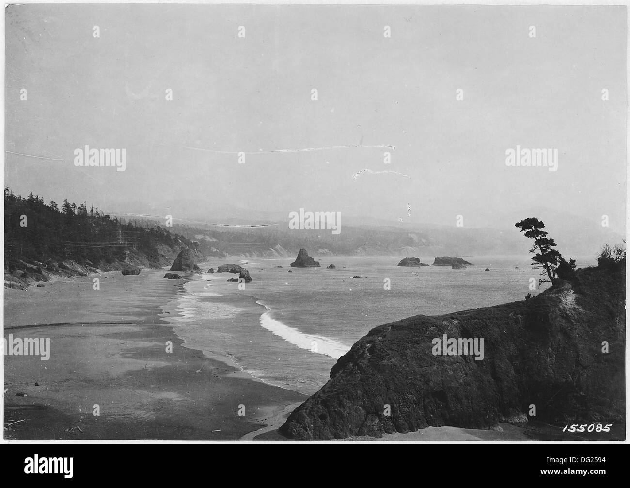 Port Orford Beach in Oregon zeigt den Battle Rock im Vordergrund und den Umatilla Forest im Hintergrund. Das Bild von 1920 zeigt die raue Schönheit der Küste und die natürliche Landschaft der Region. Stockfoto