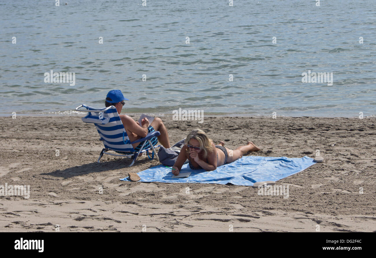 Ein Mann saß in einem Stuhl und Frau Worträtsel Sonnenbaden am Strand zu tun Stockfoto