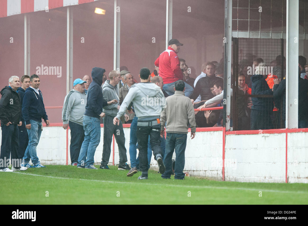 Atherstone, Warwickshire, UK. 12. Oktober 2013. Eine Gruppe von Fans aus der Heimat Ende der Sheepy-Straße Boden Spaziergang um den Umkreis des Spielfeldes und skalieren die Zäune um die besuchenden Anhänger (Barrow AFC) anzugreifen. Ein Feuerwerk wurde auch in Richtung auf der Terrasse des folgenden Weg geworfen. Eine Fahne wurde von den Barrow AFC Fans gestohlen und dann angezündet mit einem beleuchteten Feuerwerk. Atherstone Vorsitzender Rob Weale entschuldigte sich für was aufgetreten und geschworen, um die Täter zu verfolgen. Stockfoto