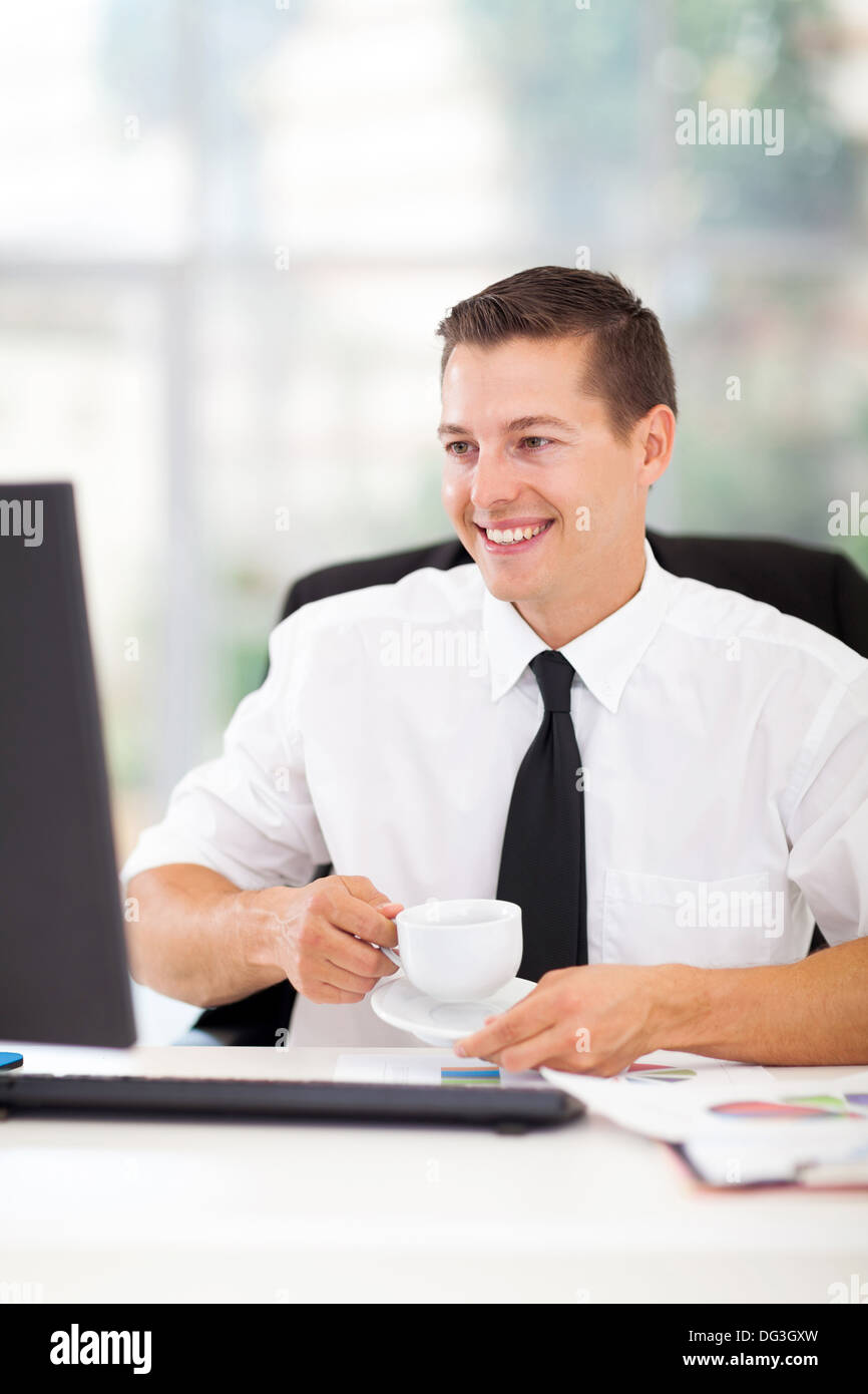 fröhliche Geschäftsmann Kaffeetrinken während der Arbeit an seinem Computer im Büro Stockfoto