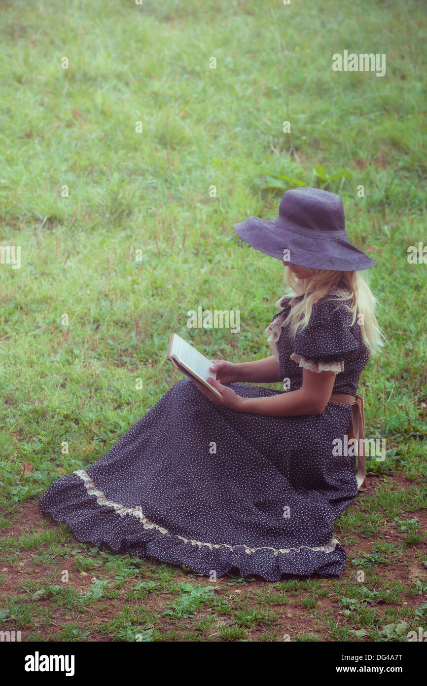 eine Frau in einem romantischen Kleid sitzt auf einem Rasen, ein Buch zu lesen Stockfoto