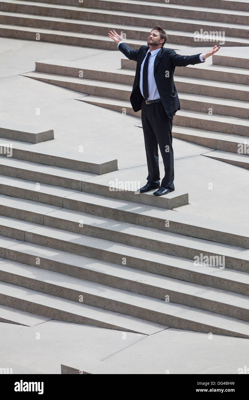 Ein Geschäftsmann Business Mann erfolgreich feiern oder deprimiert stehend Arme ausgestreckt auf den Stufen in einer Stadt Stockfoto