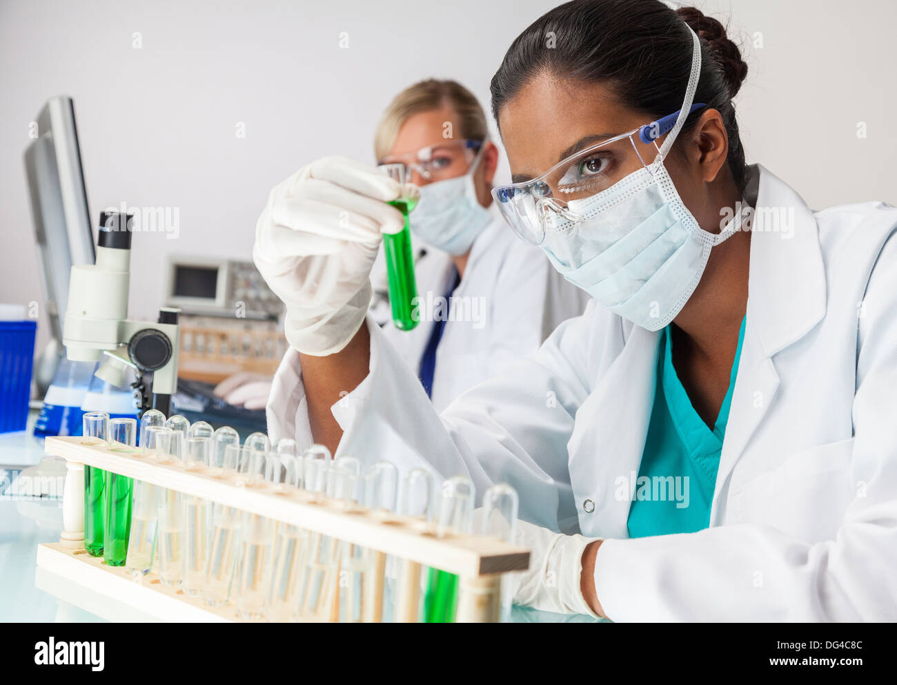 Asiatische indische medizinische oder wissenschaftliche Forscherin oder Arzt Blick auf ein Reagenzglas grüne Lösung in einem Labor Stockfoto