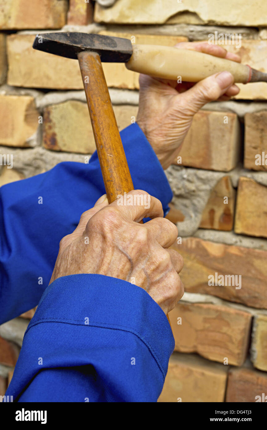 Ältere Hand mit Hammer und Meißel. Bau-Hintergrund. Stockfoto