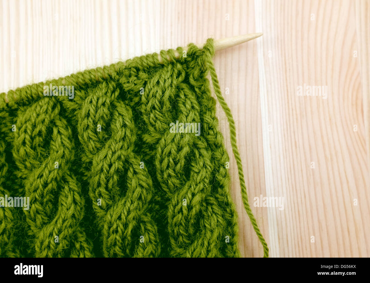 Grün gewickelt Seil Kabel stricken Masche auf der Nadel, auf einem hölzernen Hintergrund Stockfoto