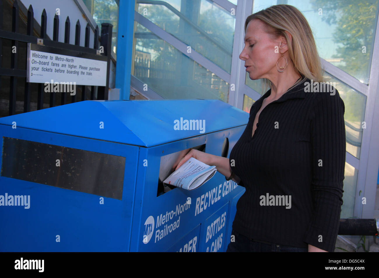 Frau recycling Zeitung in einem Papierkorb auf dem Bahnhof in den Vororten von New York City, New York, USA Stockfoto