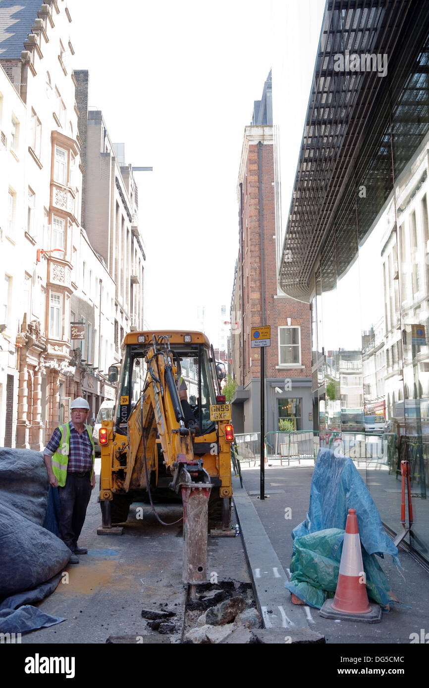 Ein Bagger Graben auf der Straße in London mit einem Baumeister in einer hohen Vis-Jacke Stockfoto