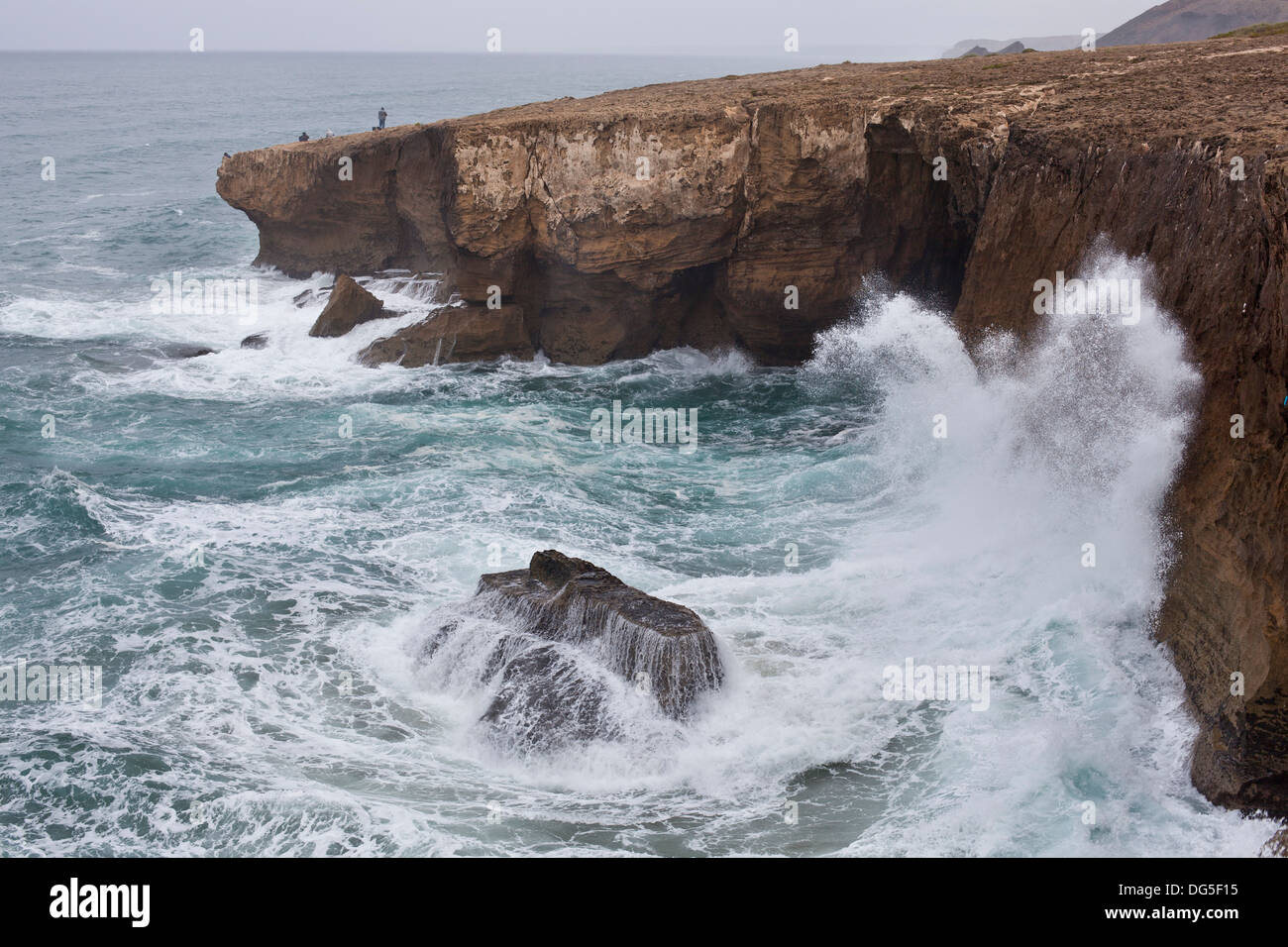 eine Welle abstürzt gegen einen Felsen, während Fischer für einen guten Fang an den Monte Clerigo Klippen an der Algarve in Portugal versuchen Stockfoto