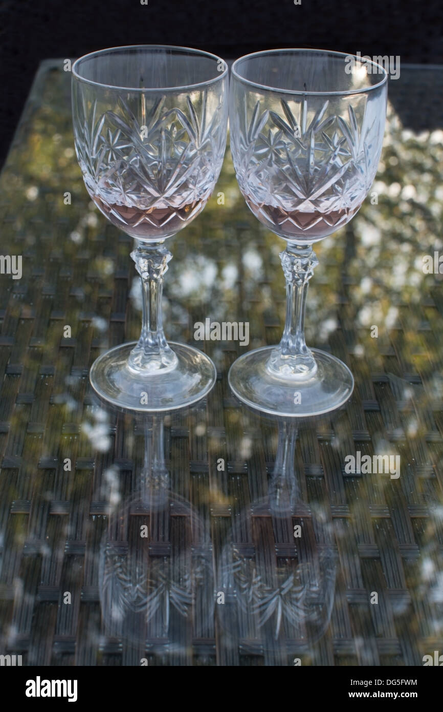 In zwei Gläser Wein Rose auf einem Rattan und Glas Tisch im Freien mit Reflexion von Bäumen. Stockfoto