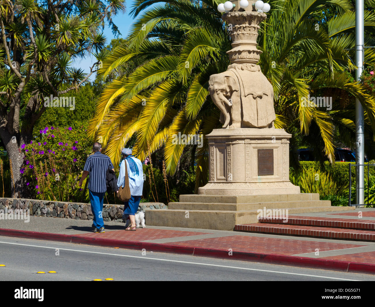 Älteres Ehepaar walking Hund vorbei an Elefanten Denkmal auf Bridgeway in Sausalito, Kalifornien Stockfoto