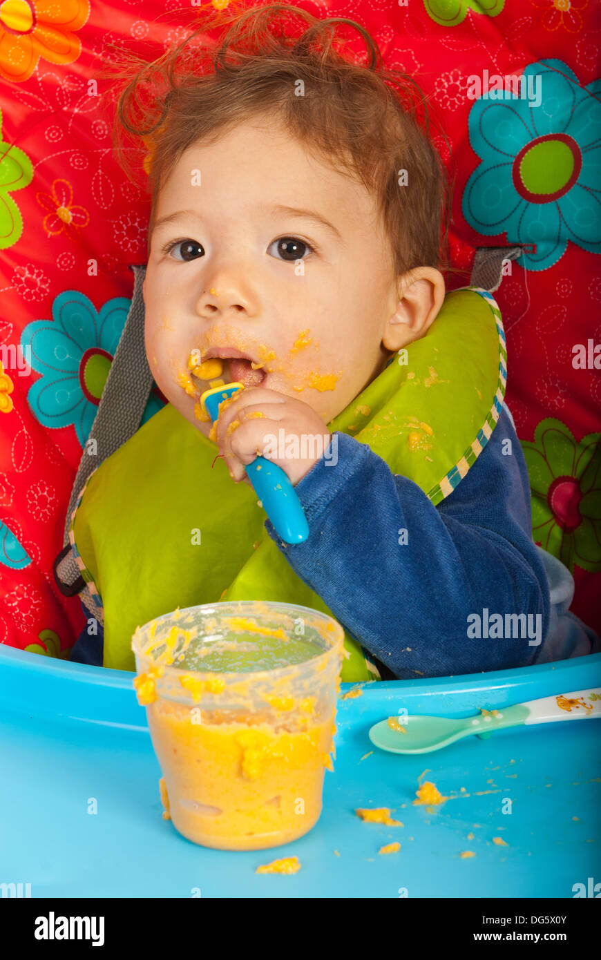 Baby Boy Verzehr von Gemüse pürieren von sich selbst und im Stuhl sitzen Stockfoto