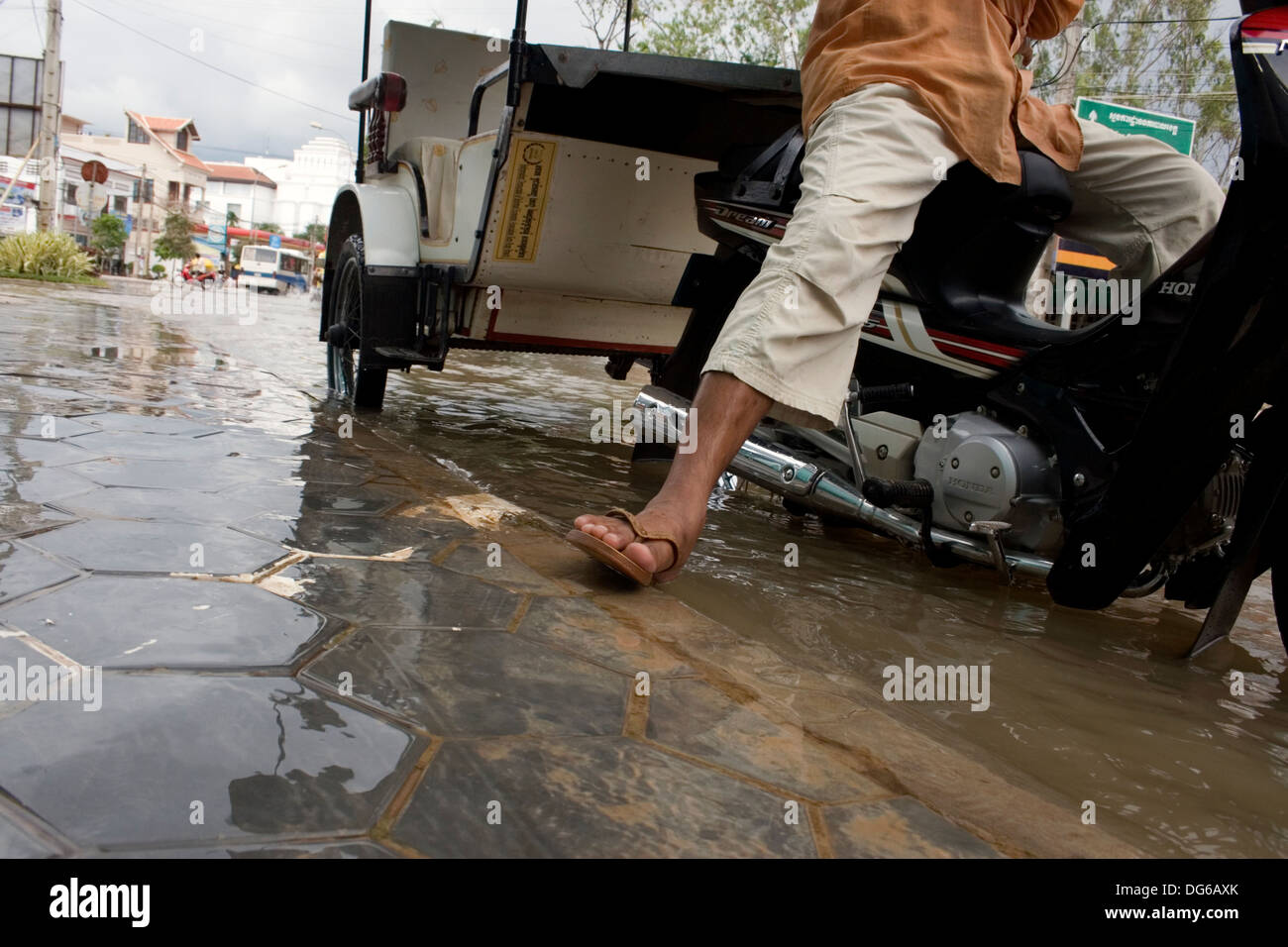 Ein Mann wartet auf Kunden in seinem einen Tuk-Tuk auf einer überfluteten Stadtstraße in Siem Reap, Kambodscha. Stockfoto