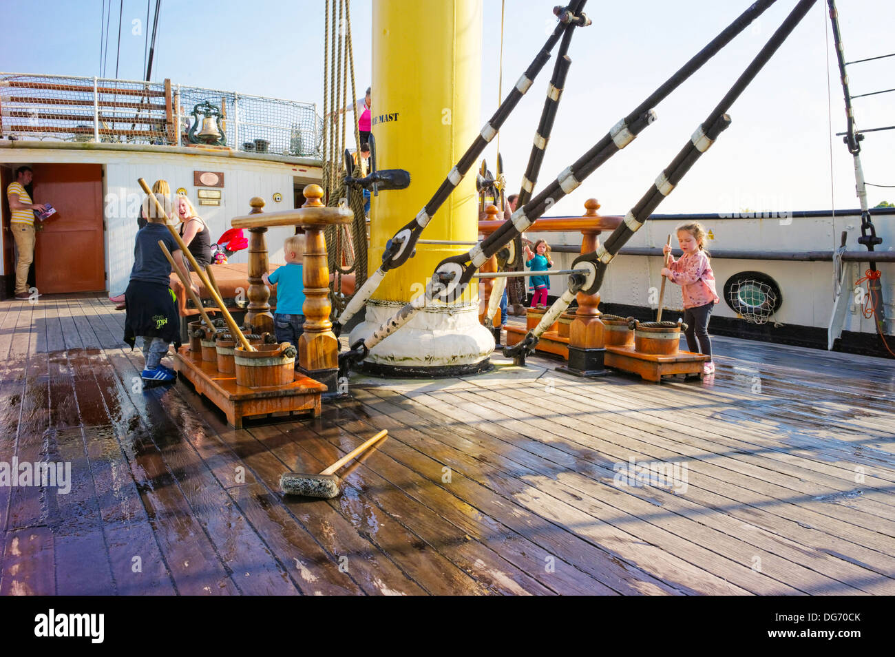 Kinder besuchen die Großsegler Glenlee probieren das Leben an Bord durch Waschen das Deck mit Wasser und Bürsten von den Eltern beobachtet Stockfoto