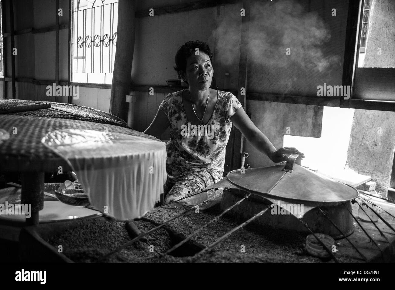 Eine vietnamesische Frau sitzt durch einen glühenden Ofen, während sie Hunderte von Reis Papier macht. Stockfoto