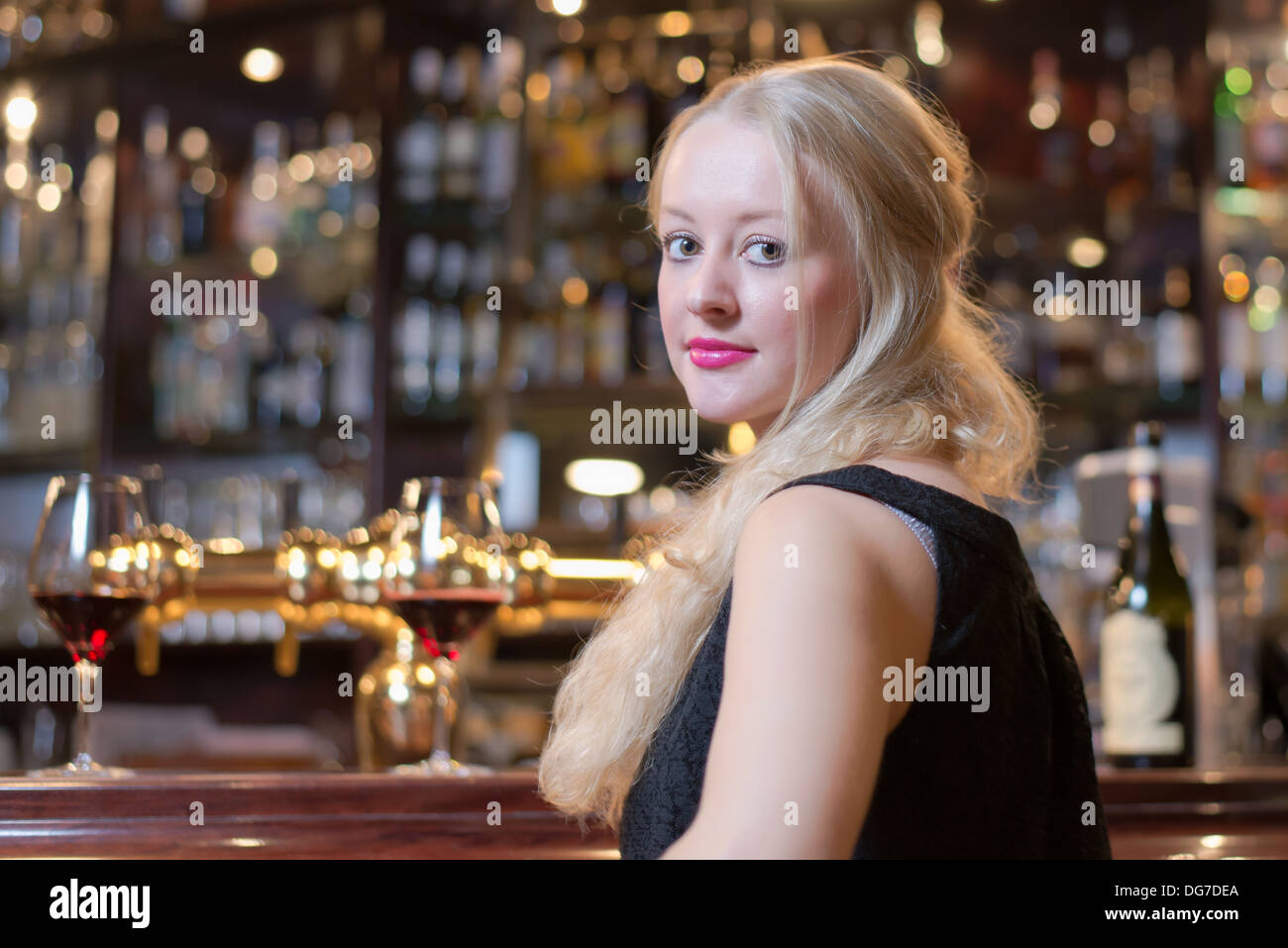 Schöne junge blonde Frau in einer Bar sitzt zu begegnen in einem gehobenen Hotel, Club oder Restaurant Blick zurück über die Schulter Stockfoto