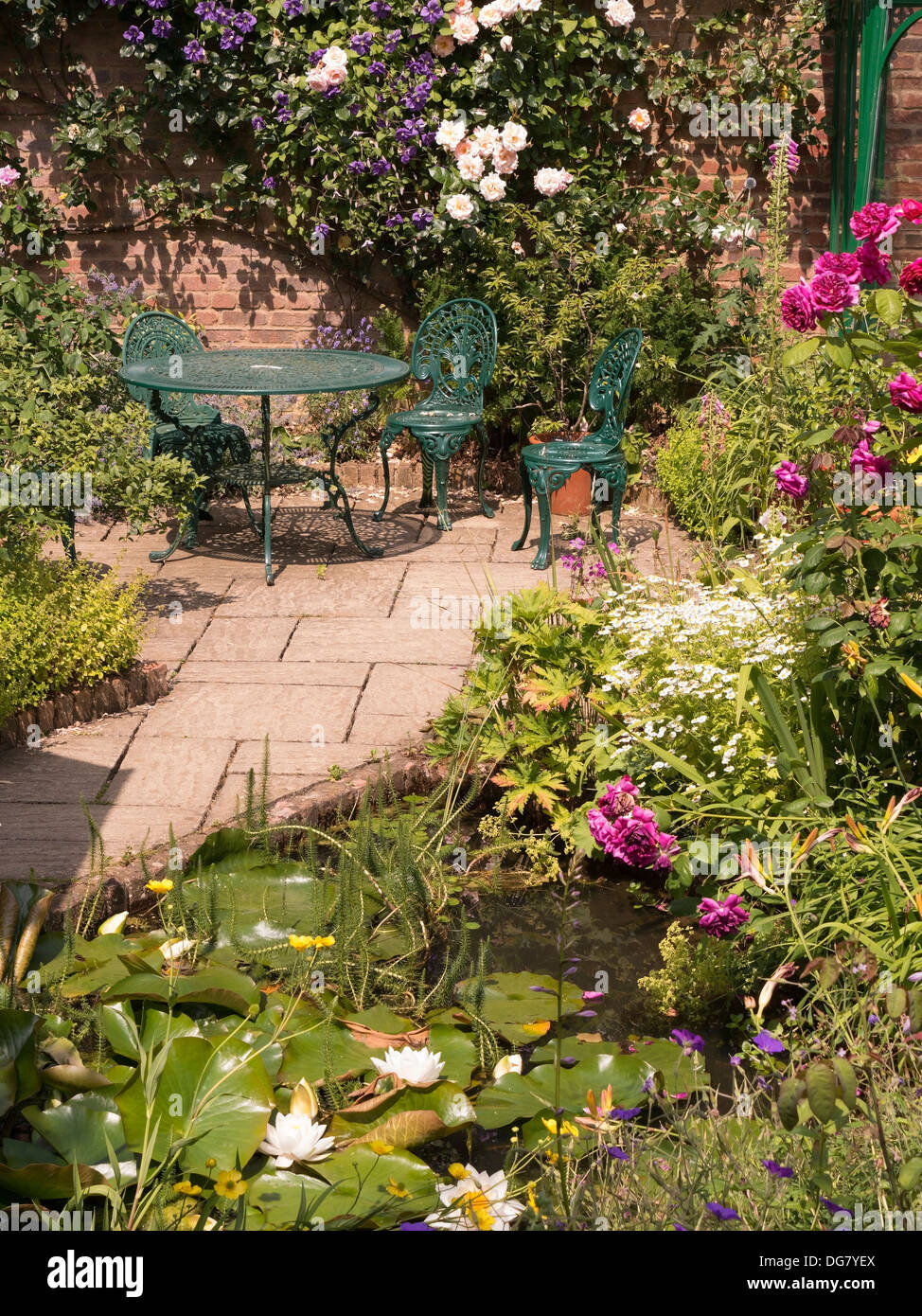 Attraktive gepflastert sonnigen Gartensitzplatz mit Tisch und Stühlen und Teich, Barnsdale Gärten, Oakham, Rutland, England, UK. Stockfoto