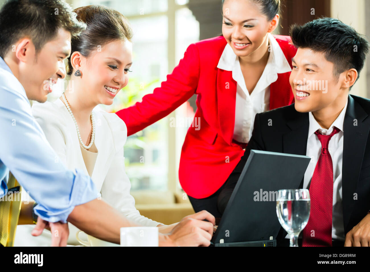 Vier chinesische asiatische Geschäftsleute und Frauen, die Treffen in einem Hotel lobby Blick auf Dokumente auf Laptop und Kaffee trinken Stockfoto