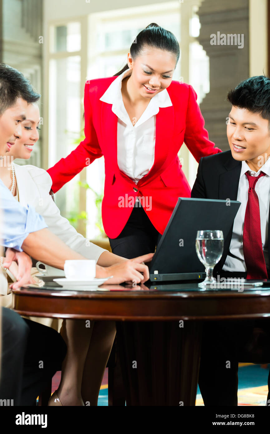 Vier chinesische asiatische Geschäftsleute und Frauen, die Treffen in einem Hotel lobby Blick auf Dokumente auf Laptop und Kaffee trinken Stockfoto