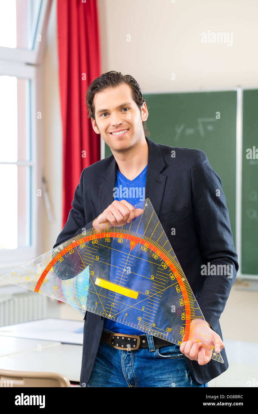 Lehrer oder Dozent in der Schule hält ein Geometrie-Dreieck vor einer Tafel in der Schulklasse Stockfoto