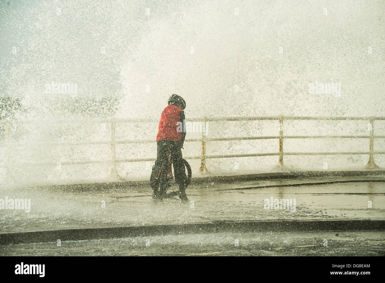 Aberystwyth, Wales, UK. 16. Oktober 2013.  Starke Winde und stürmische See bringen riesige Wellen zerschlagen die Promenade und den Hafen in Aberystwyth an der Westküste Wales, UK. Ein junger Radfahrer wird von den Wellen getränkt, da er entlang der Strandpromenade-Zyklen. Bildnachweis: Keith Morris/Alamy Live-Nachrichten Stockfoto