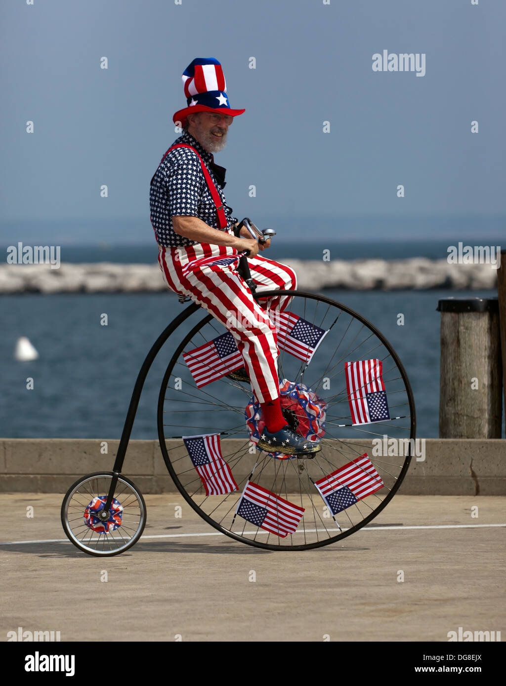 Mann gekleidet in einem patriotischen amerikanischen Kostüm, ein moderner Penny Farthing Fahrrad am Ende der MacMillan Pier fahren. Stockfoto