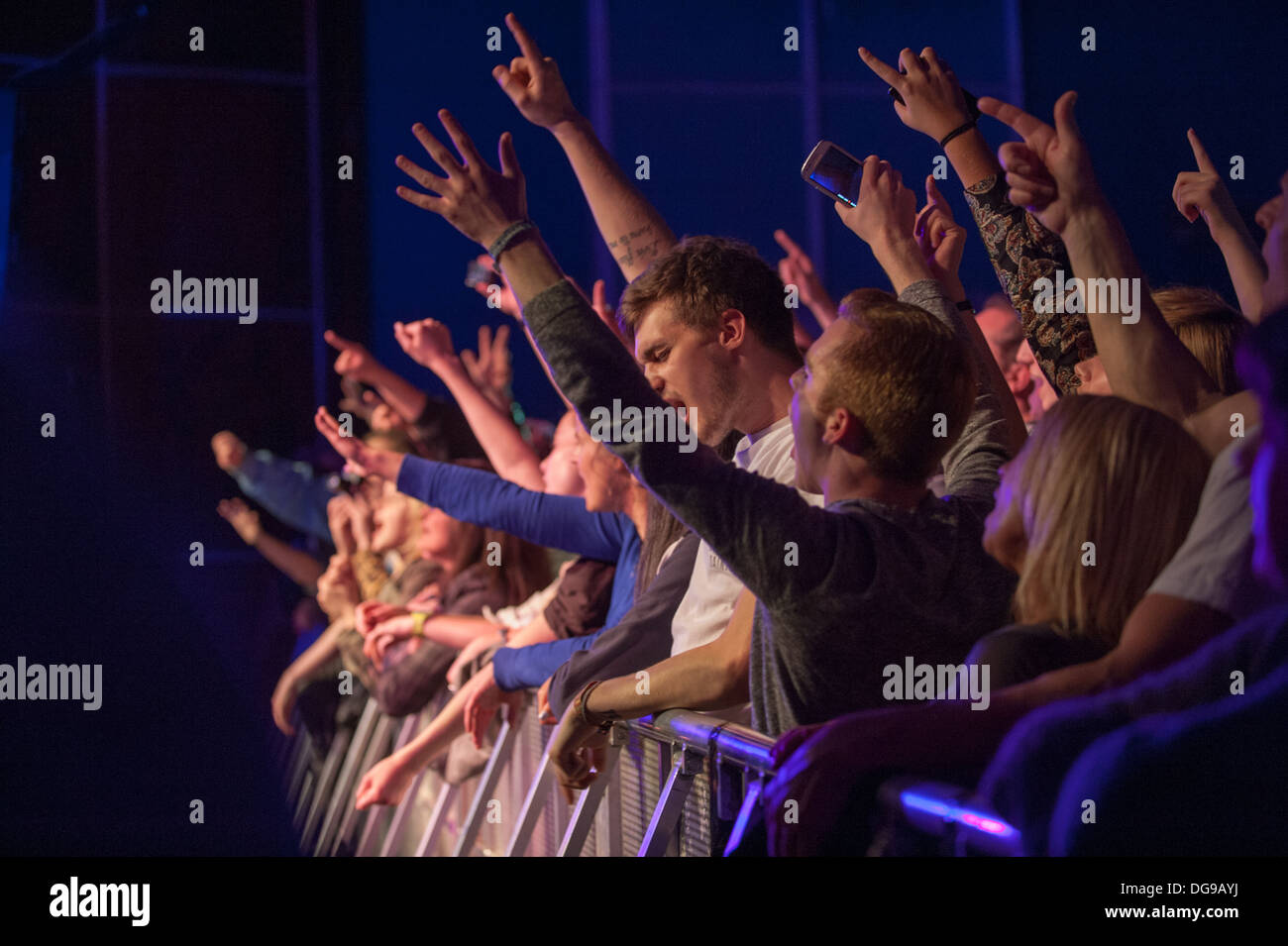 Junge Musikfans bei einem Live-Gig zerdrückten sich an der Vorderseite der Bühne gegen die Schranke und jubelten, klatschten und schrien bei einer Band auf der Bühne Stockfoto