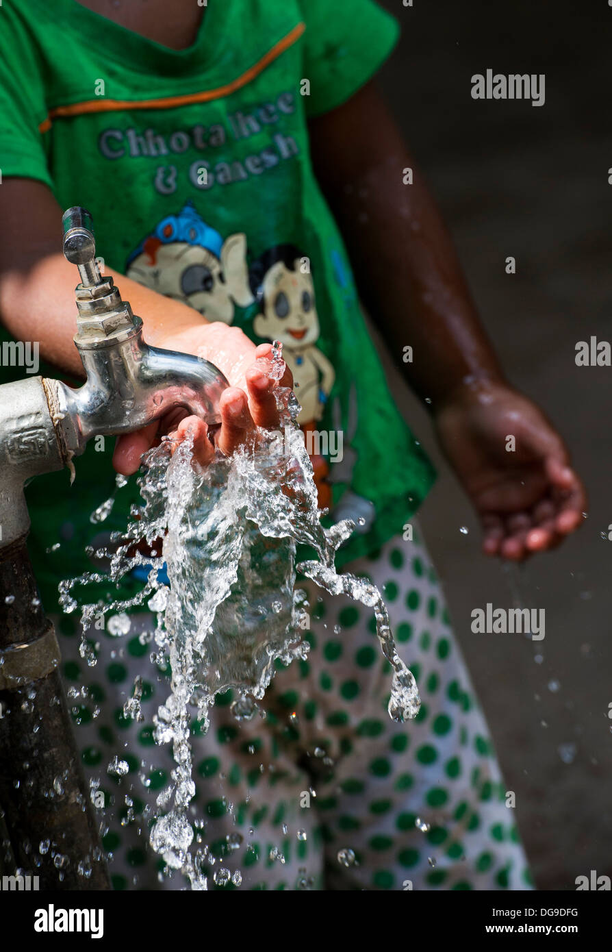 Junge Inderin / Kleinkinder spielen mit Wasser aus einem Hahn in einem indischen Dorf. Andhra Pradesh, Indien Stockfoto
