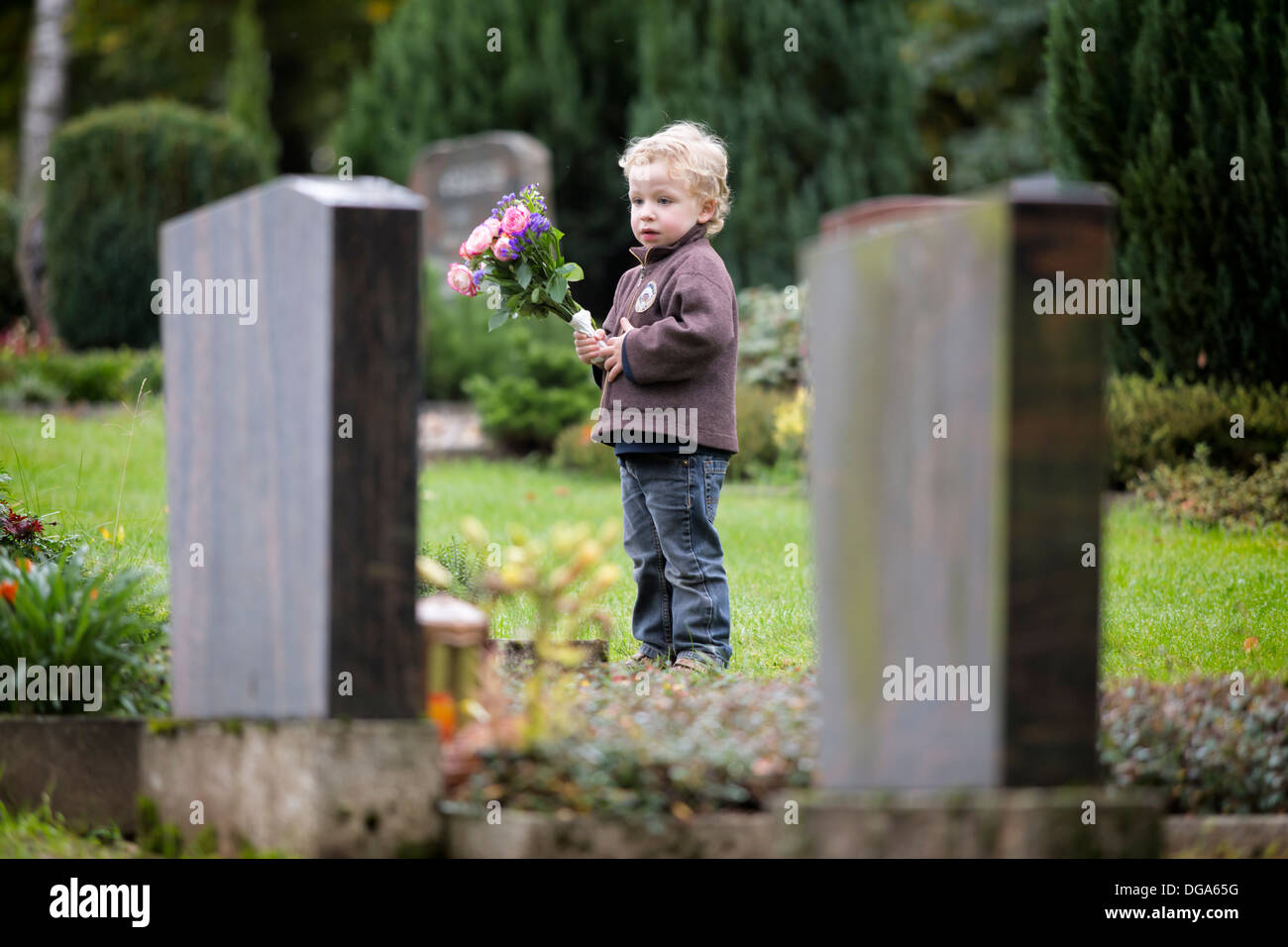 Junge, 3 Jahre, mit Blumen an einem Grab auf einem Friedhof Stockfoto