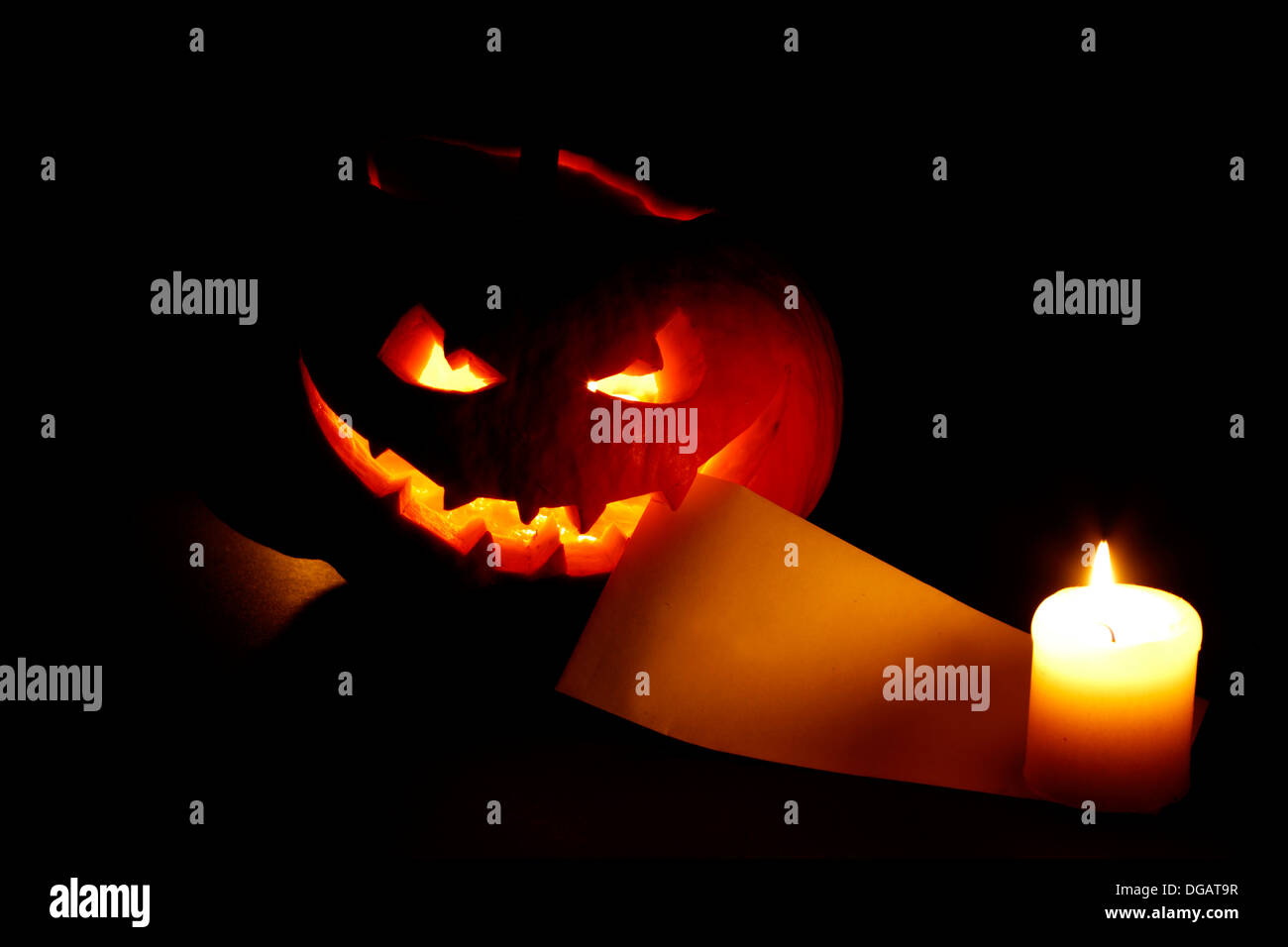 Halloween-Kürbis mit brennender Kerze und Postkarte auf schwarzem Hintergrund Stockfoto