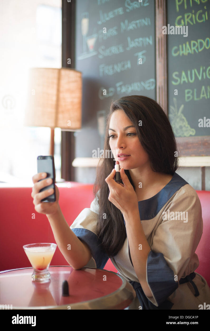 Mitte Erwachsene Frauen mit Handy, Lippenstift im Restaurant anwenden Stockfoto