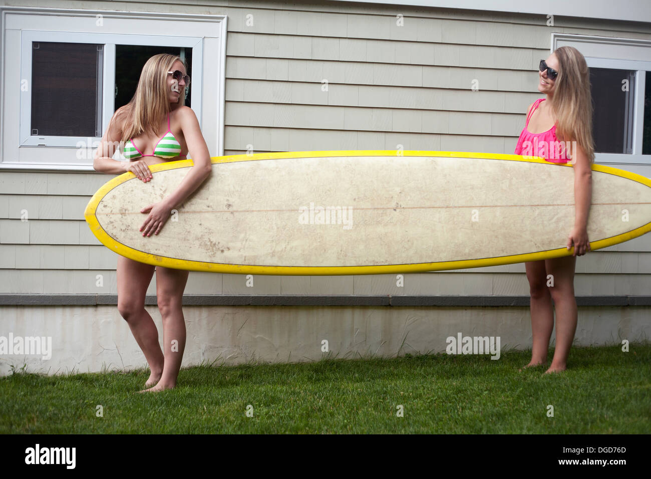 Junge Frauen tragen Surfbrett auf dem Rasen Stockfoto