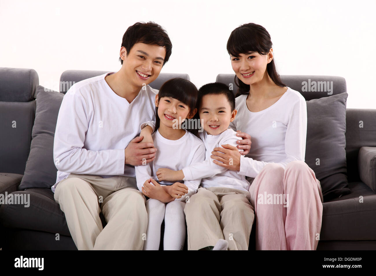 East Asian-Familie mit zwei Kindern, auf dem Sofa sitzen, Lächeln, in die Kamera schaut Stockfoto