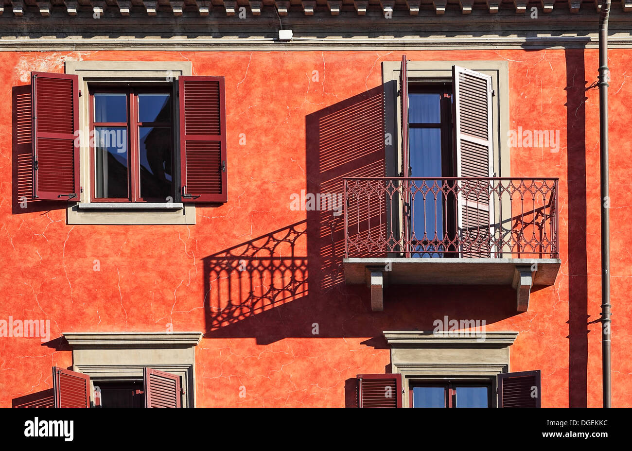 Balkon und hölzernen Fensterläden auf Windows werfen Schatten auf die Fassade des Hauses mit roten Wand an sonnigen Tag in Stadt von Alba, Italien Stockfoto