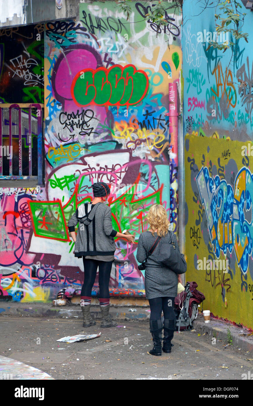 Junge Frau sprühen Graffiti auf Straße Wand von Freund beobachtet Stockfoto