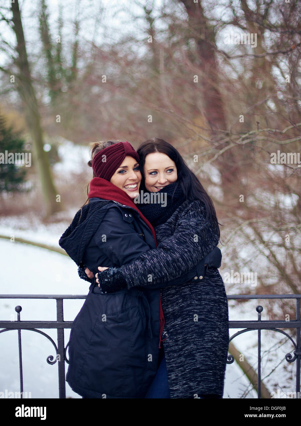 Fröhlich Schwestern umarmen einander draußen im kalten Winter park Stockfoto