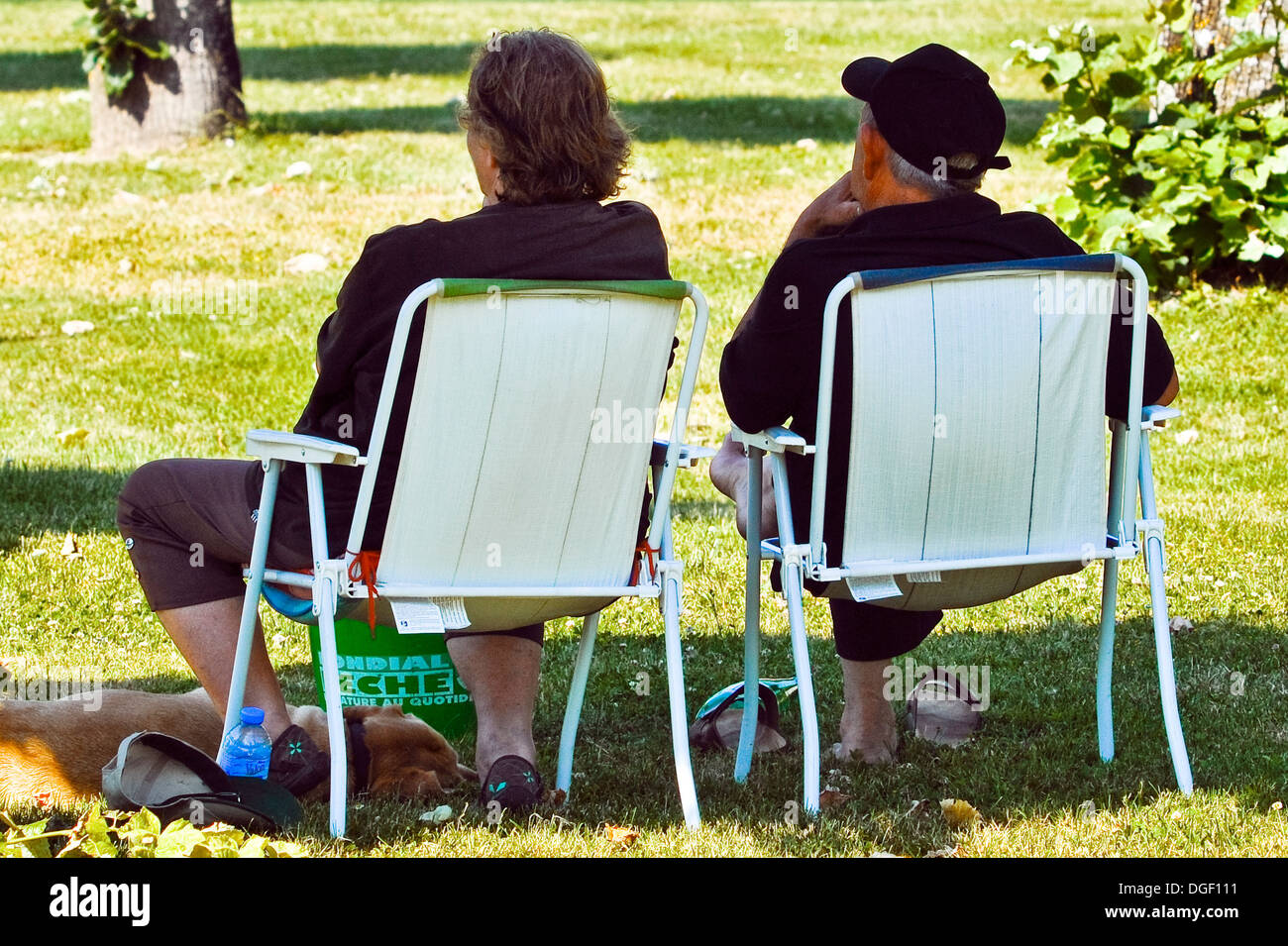 Rückansicht des Paares / Mann und Frau sitzen auf Klappstühlen im öffentlichen Park - Frankreich. Stockfoto