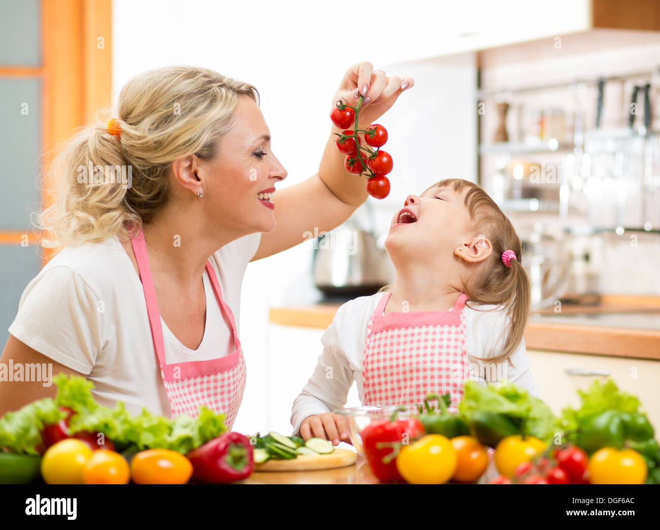 Mutter Vorbereitung Abendessen und Fütterung Kind Tomate in Küche Stockfoto