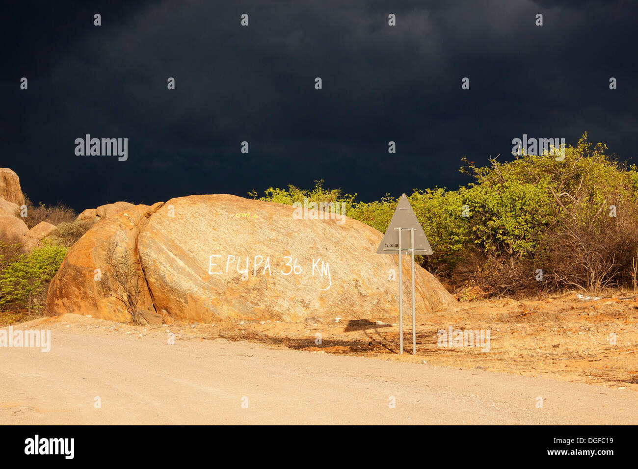 Dunkle Sturmfront über Felsen mit Schild "Epupa 36 km", Kaokoland, Kunene, Namibia Stockfoto