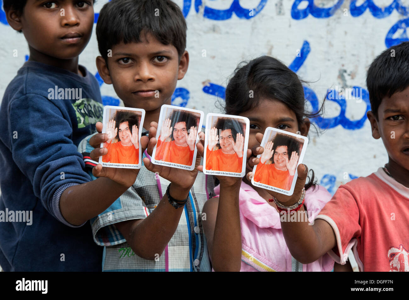 Vier indische Kinder hochhalten Fotos von Sri Sathya Sai Baba in einem indischen Dorf. Andhra Pradesh, Indien Stockfoto