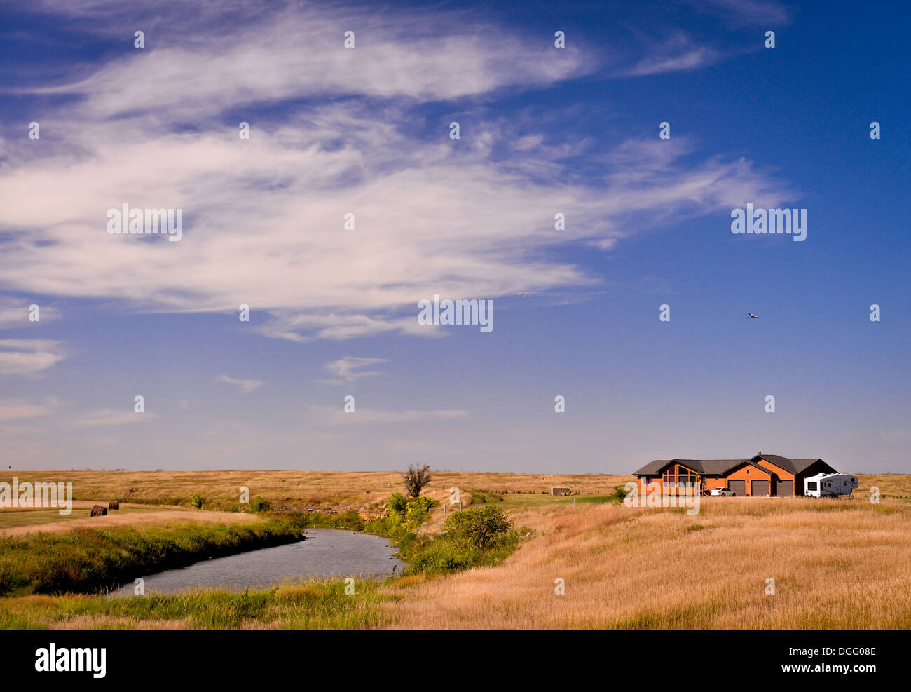 Ein Haus auf eine Prärie an einem See unter einem lebhaften blauen Himmel Stockfoto