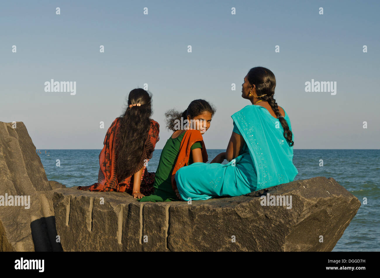 Drei junge Damen sitzen auf einem Felsen am Strand von Pondicherry, Blick auf das Meer, Pondicherry, Indien, Asien Stockfoto