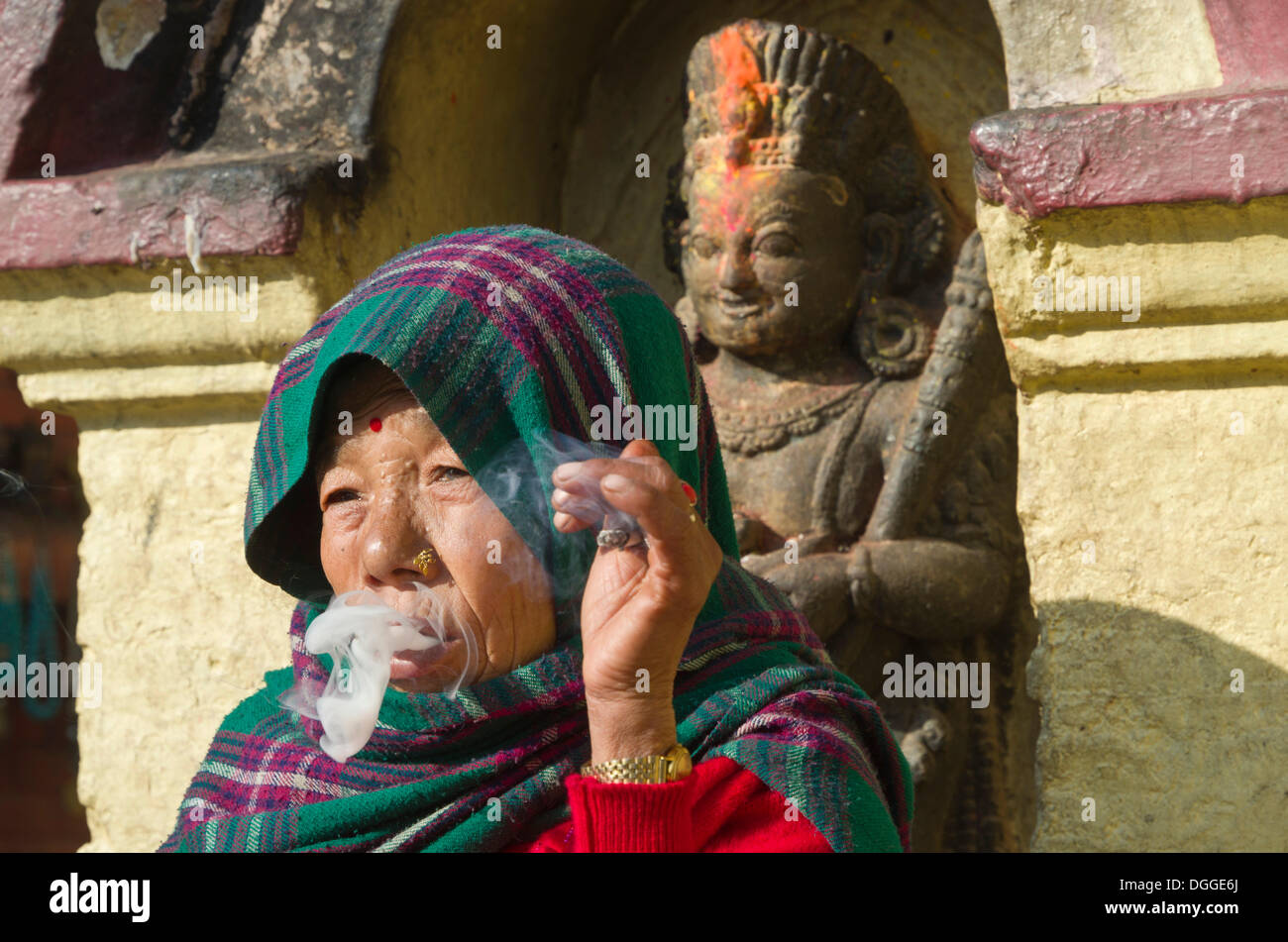 Alte Frau, Rauchen, vor einer Statue, Kathmandu, Kathmandu District, Bagmati Zone, Nepal Stockfoto
