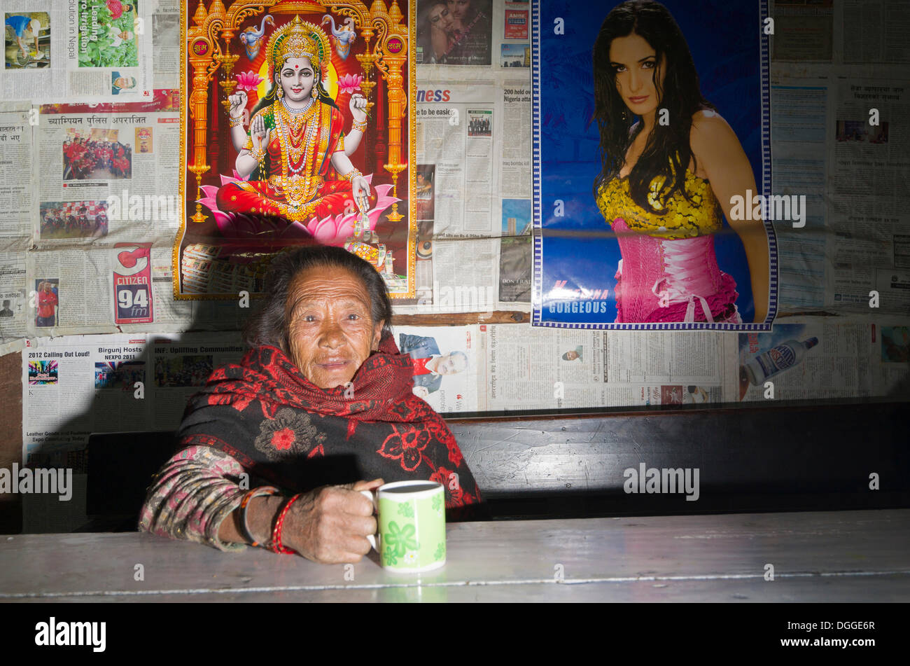 Alte Frau trinkt Tee in einem lokalen Restaurant, einige Poster an der Wand hinter Shivalaya, Solukhumbu Bezirk, Sagarmāthā Zone Stockfoto